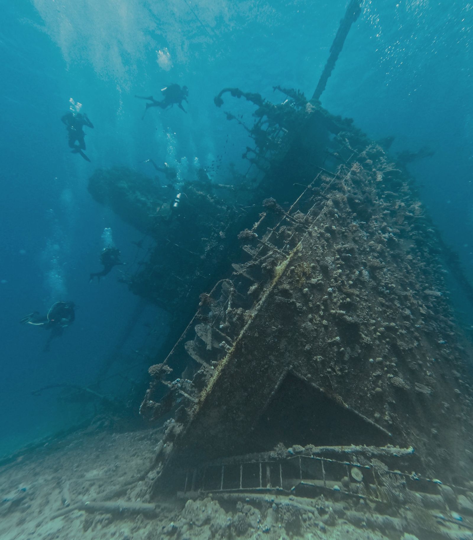 A dive team descending onto a large shipwreck, its superstructure rising out of the blue
